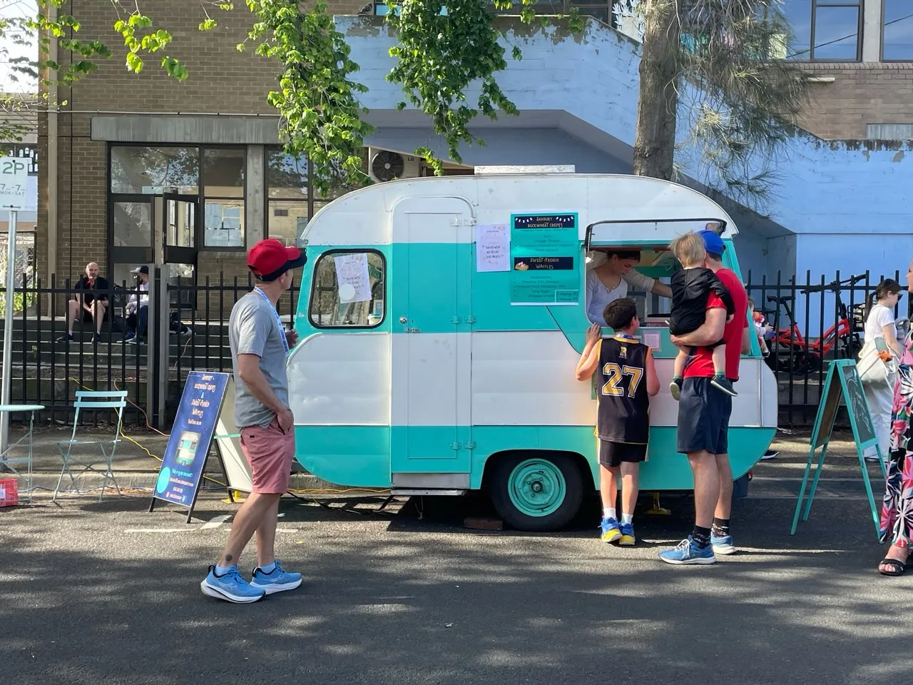 Customers queuing at the turquoise French food caravan at a sunny outdoor street market